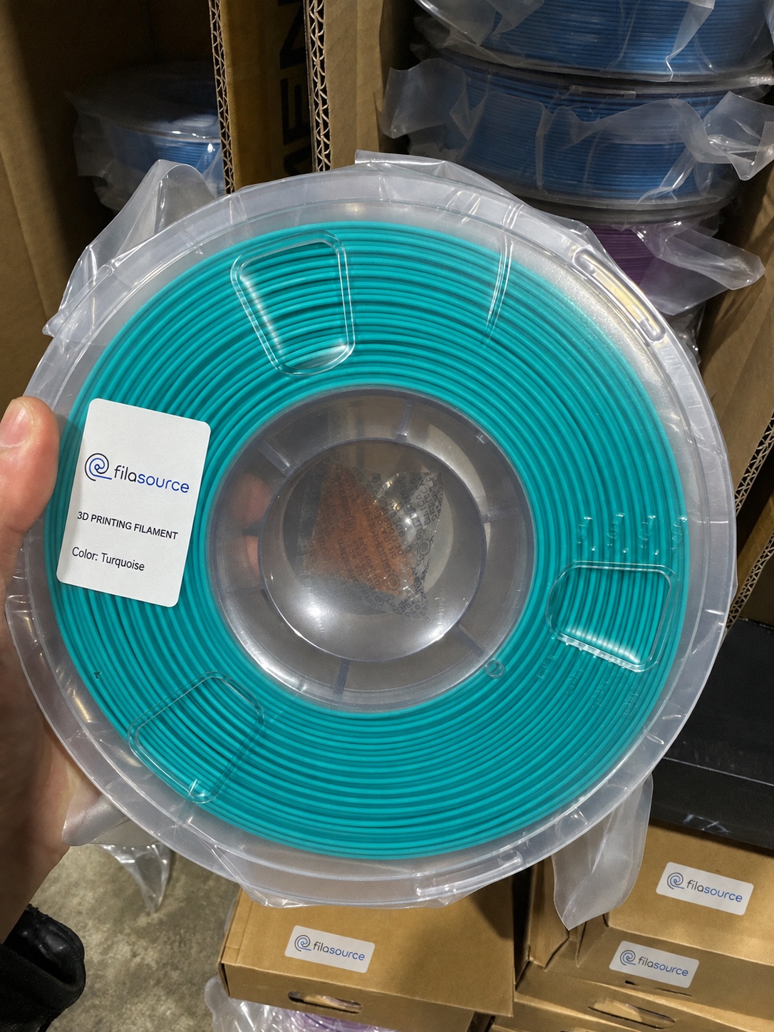 Teal filament spool in a clear protective bag.